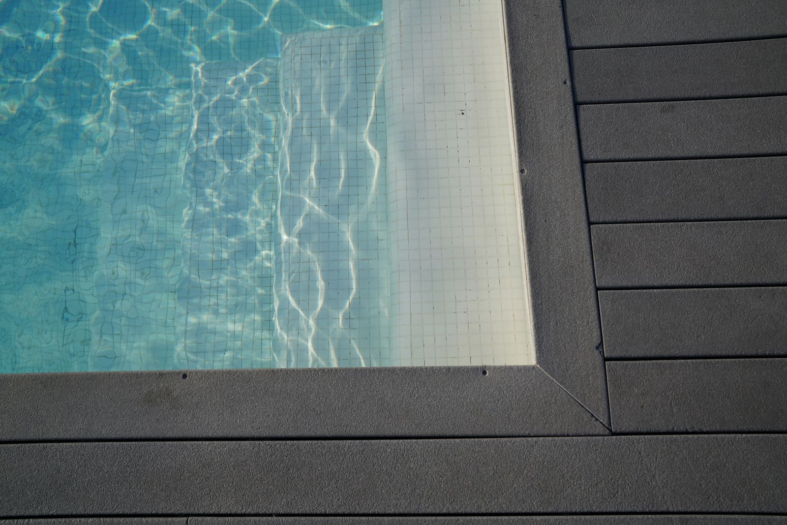 AI-generated illustrative image of a textured light grey concrete surround bordering a swimming pool