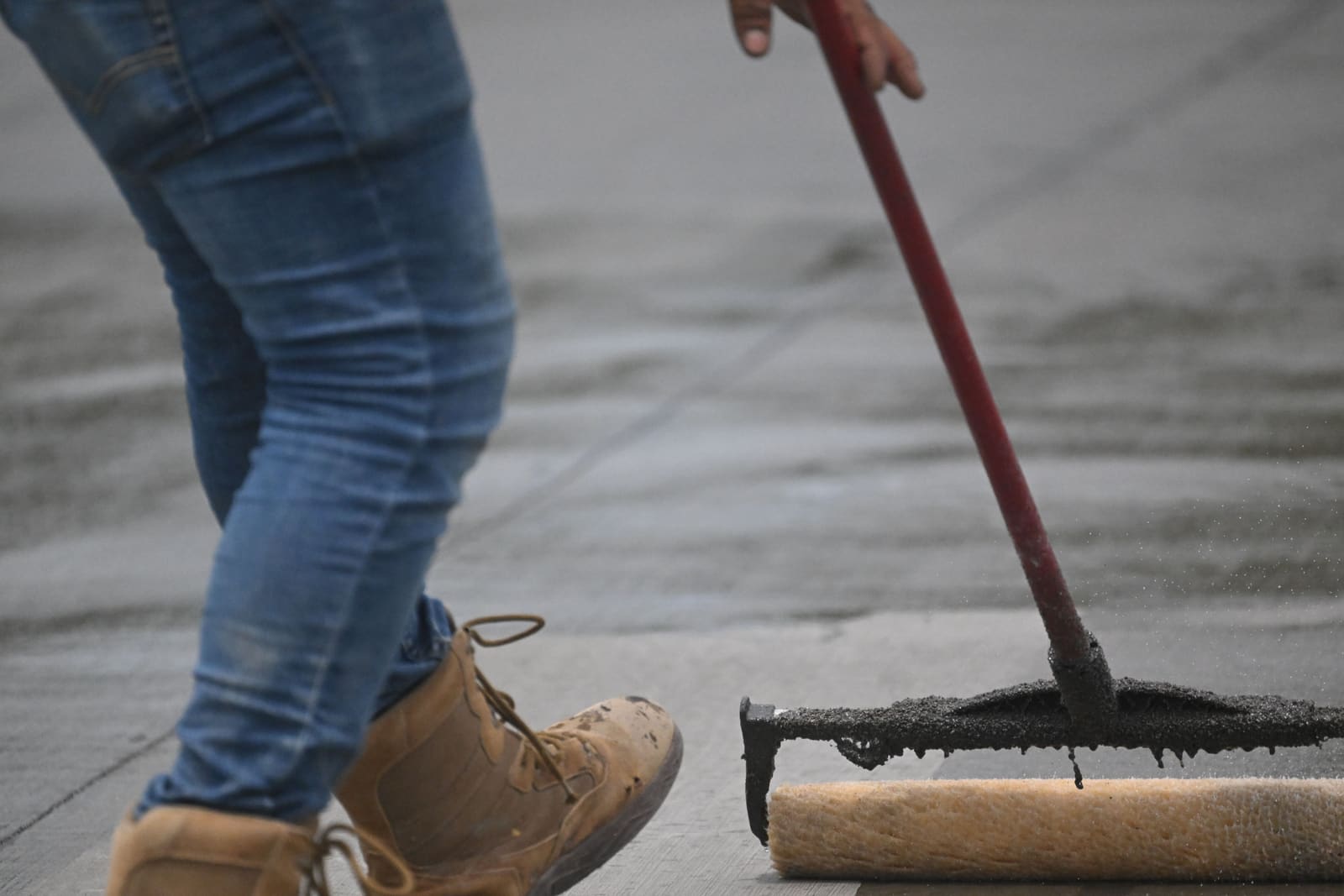 AI-generated illustrative image of coastal-grade sealer being applied to a concrete driveway with a roller